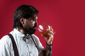 handsome hipster drinking rum glass. party goer with alcohol. brandy or cognac. bearded man in suspenders drink scotch whiskey. brutal guy bartender wear bow tie. elegant male barman. copy space