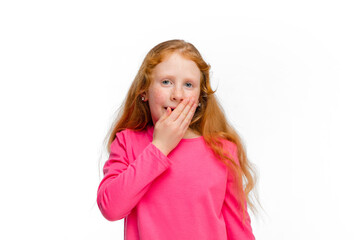 Shocked, covering mouth with hand. Happy, smiley redhair girl on white studio background with copyspace for ad. Looks happy, cheerful. Childhood, education, human emotions, facial expression concept.