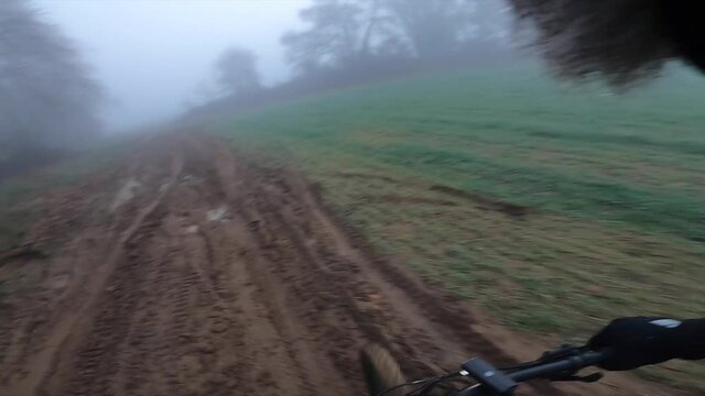 Riding a mountain bike on a muddy gravel path on a green foggy landscape