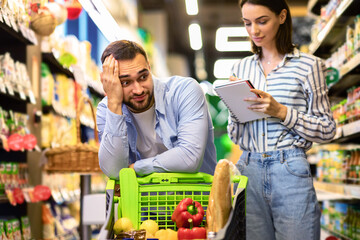 Funny young couple with shopping list in supermarket