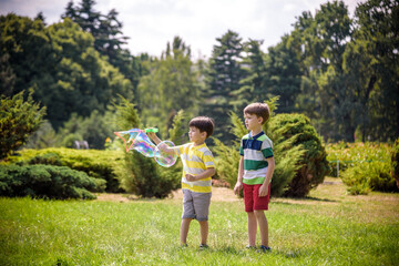 Boy blowing soap bubbles while an excited kid enjoys the bubbles. Happy teenage boy and his brother in a park enjoying making soap bubbles. Happy childhood friendship concept