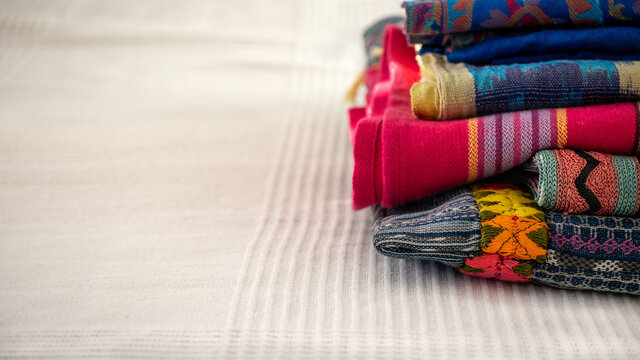 Piled original vibrant multicolored ethnic hand woven textiles from Southern America, India: pink, blue, yellow  on a white cloth background. Fair trade concept. Close up.