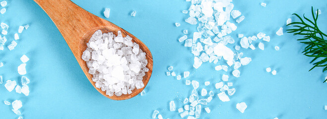 Coarse salt crystals on a blue table. Wooden spoon with sea salt. Background for advertising salty....