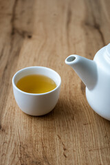 Eine Tasse Kräutertee und eine weiße Teekanne auf einem braunen Holz Tisch. Minimalistisch, pause machen.