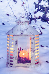 White vintage lantern with candles in a snowy garden in the evening light, vertical