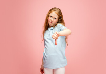 Fototapeta na wymiar Thumb down, dislike. Happy, smiley redhair girl isolated on pink studio background with copyspace for ad. Looks happy, cheerful. Childhood, education, human emotions, facial expression concept.