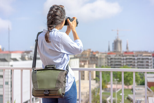 Woman taking a picture with her camera at a touristic place with a photo bag on her shoulder.