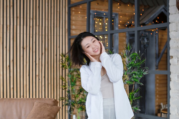 Portrait of a beautiful Asian young woman in a white fashionable shirt at home in a dark loft design interior.