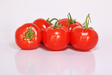 Five bright red tomatoes with green stems on a white background.