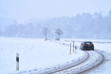 Auto auf Schneebedeckter kurviger Straße bei Schneesturm im Winter mit Brücke und Wald am Horizont