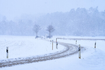 Schneebedeckte kurvige Landstra&szlig;e bei Schneesturm im Winter mit Br&uuml;cke und B&auml;umen