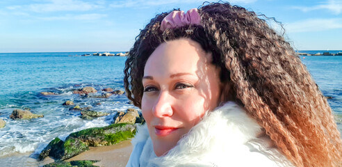 Portrait of a beautiful woman with curly hair on background of the blue waters of the Mediterranean sea in Barcelona, Spain