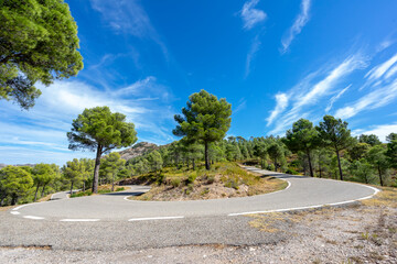 Curvy mountain road under a blue sky with scattered clouds on a summer day (no cars)