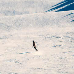 Lone snowboarder riding down a steep slope at an alpine sports resort.