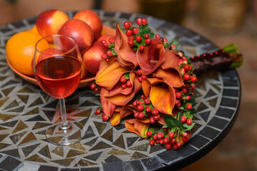 Bright, orange bridal bouquet of calla flowers on a table with a glass of champagne and fruits.