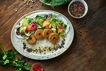Appetizing salad in the style of oriental cuisine. Fresh vegetable salad with falafel and olive oil served in a blue plate on a wooden background. Restaurant food