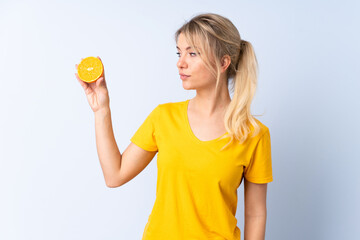 Blonde woman over isolated blue background holding an orange