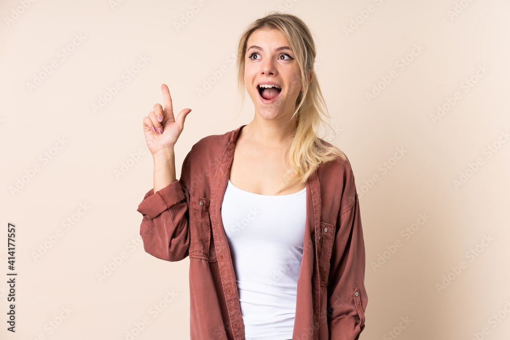 Wall mural blonde woman over isolated background pointing up and surprised