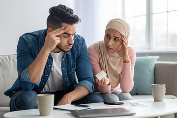 Confusded lady in hijab showing bill her upset husband
