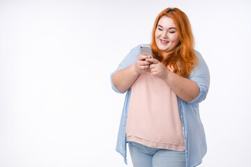 Portrait of a young red-haired plump woman using phone isolated in white