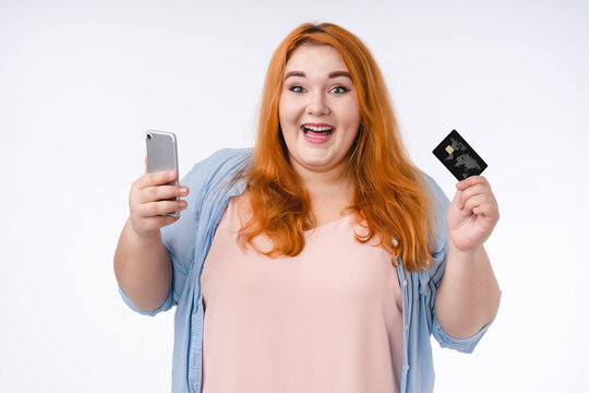 Adorable young corpulent woman holding smart phone and credit card isolated over white background