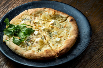 Wood-fired pizza with 4 types of cheese and white sauce with crispy sides, served on a black plate on a wooden background. pizzette a kind of Italian pizza