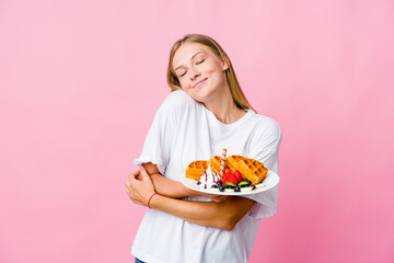 Young russian woman eating a waffle isolated hugs, smiling carefree and happy.