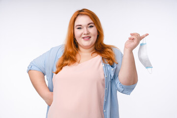 Plump woman with ginger hair put down her protective mask against coronavirus isolated over white background