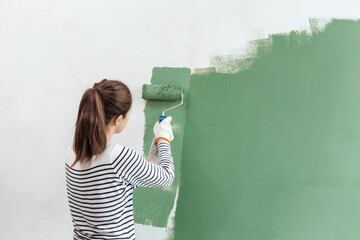 Young woman is painting the wall into green with paint roller in new house