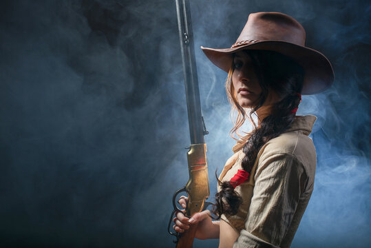 Portrait of a beautiful brunette cowgirl with a rifle on a background of smoke