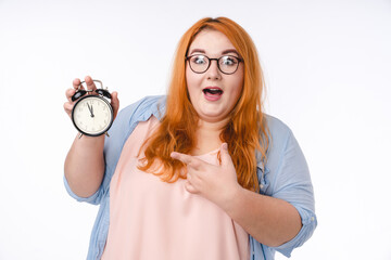 Surprised plus size woman pointing at clock showing 11:55 time isolated in white