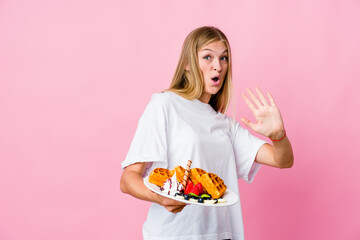 Young russian woman eating a waffle isolated being shocked due to an imminent danger