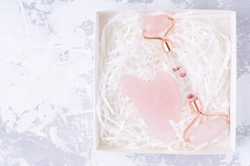 Pink Gua Sha massage tool in box on a white cement background, top view. Rose Quartz jade roller
