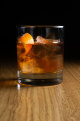Old fashion - an alcoholic cocktail based on bourbon, scotch or rye whiskey decorated with orange zest in a transparent glass on a wooden table
