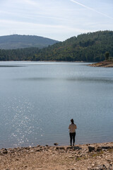 Fototapeta na wymiar Caucasian girl looking at the lake water of Apartadura dam with mountains with trees landscape in Alentejo, Portugal