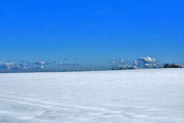 Fototapeta na wymiar Je zur Hälfte eine mit Schnee bedeckte weiße Fläche vor tiefblauem Himmel