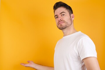 Portrait of young handsome Caucasian man holding a salad bowl against yellow wall  with arm out in a welcoming gesture.