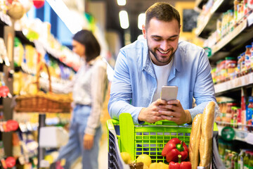 Young guy with mobile phone shopping at super market