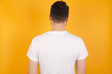 young handsome Caucasian man holding a salad bowl against yellow wall standing backwards looking away with arms on body.