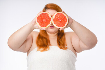 Fat young woman in spa towel with grapefruits on her face isolated over white background