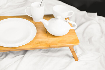 Wooden tray with with dishes and book near soft blanket on bed. tray with dishes in bed. Flat lay top-down. romance