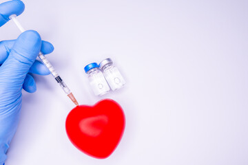 a hand in a medical glove holds an ampoule containing the covid-19 vaccine, invented to prevent the spread of the virus around the world. mask with a red heart on a white background