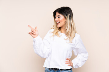 Teenager girl isolated on beige background pointing finger to the side and presenting a product