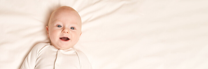 Cute small boy lying at bed. Childhood concept. Light background. Smiling child. Happy emotion. Copyspace. Stay home. Mockup. Horizontal banner