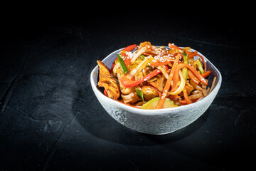 Udon stir-fry noodles with chicken and vegetables on dark background. Appetizing asian cuisine