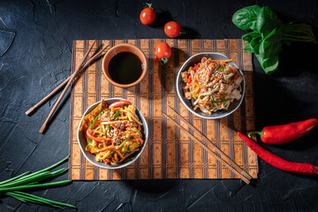 Udon noodles with fried chicken, shrimps (prawns) and vegetables on dark background
