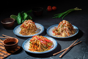 Udon noodles with fried chicken, shrimps (prawns) and vegetables on dark background