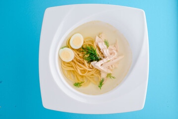 broth with noodles, chicken and egg on a white plate on a blue background. close-up. photo for clipping. for the menu
