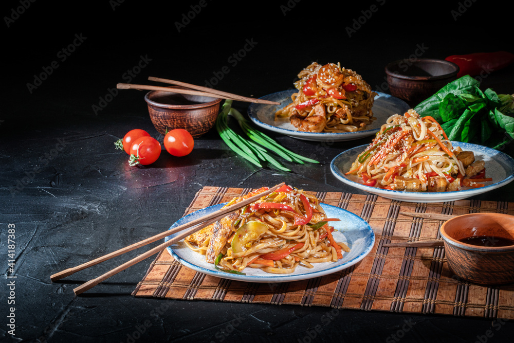 Wall mural udon noodles with fried chicken, shrimps (prawns) and vegetables on dark background