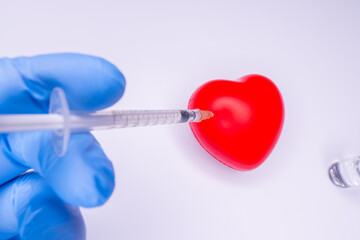 a hand in a medical glove holds an ampoule containing the covid-19 vaccine, invented to prevent the spread of the virus around the world. mask with a red heart on a white background